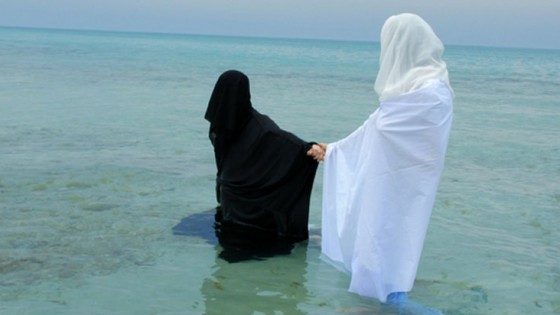 woman in black robe holding hand of woman in white robe in body of water
