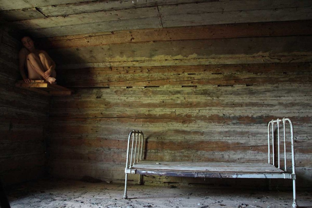 empty bed with no mattress and woman hiding in the shadows