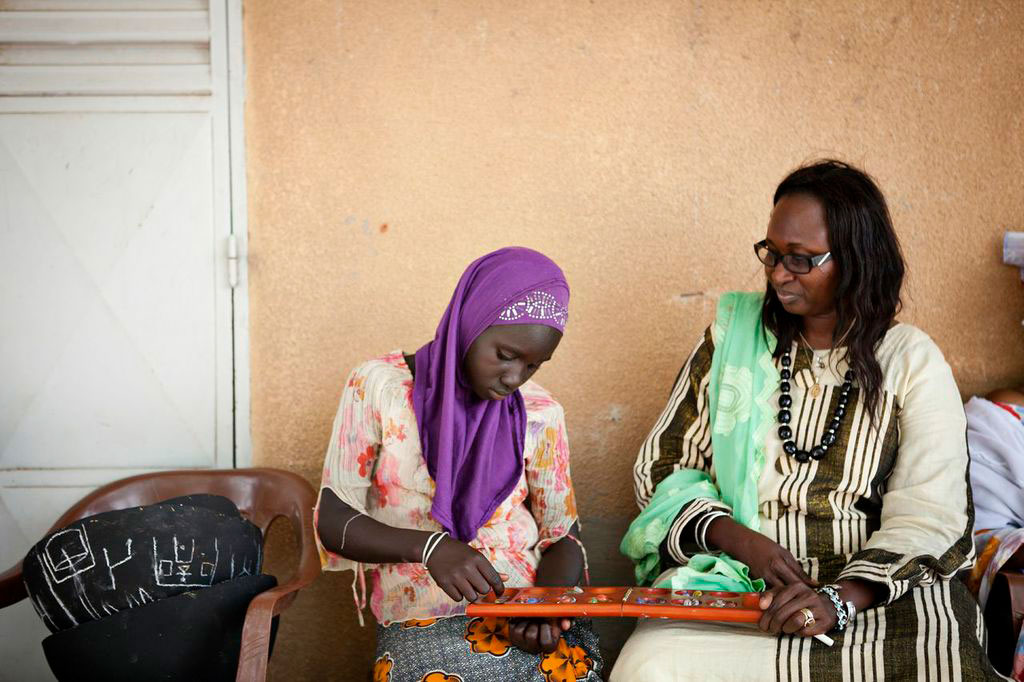 student in Senegal playing oware game while teacher looks on