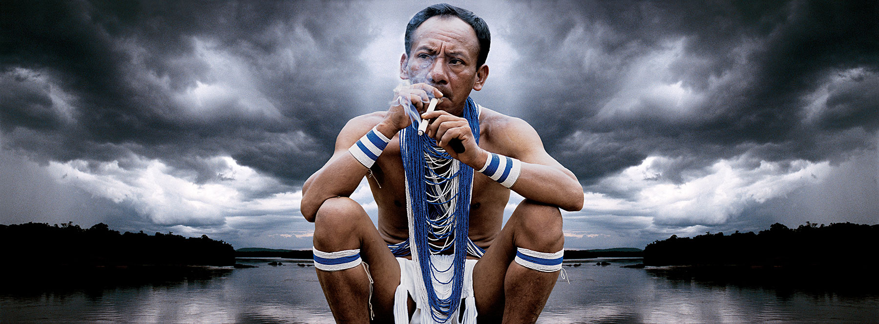 indigenous man smoking in front of lake