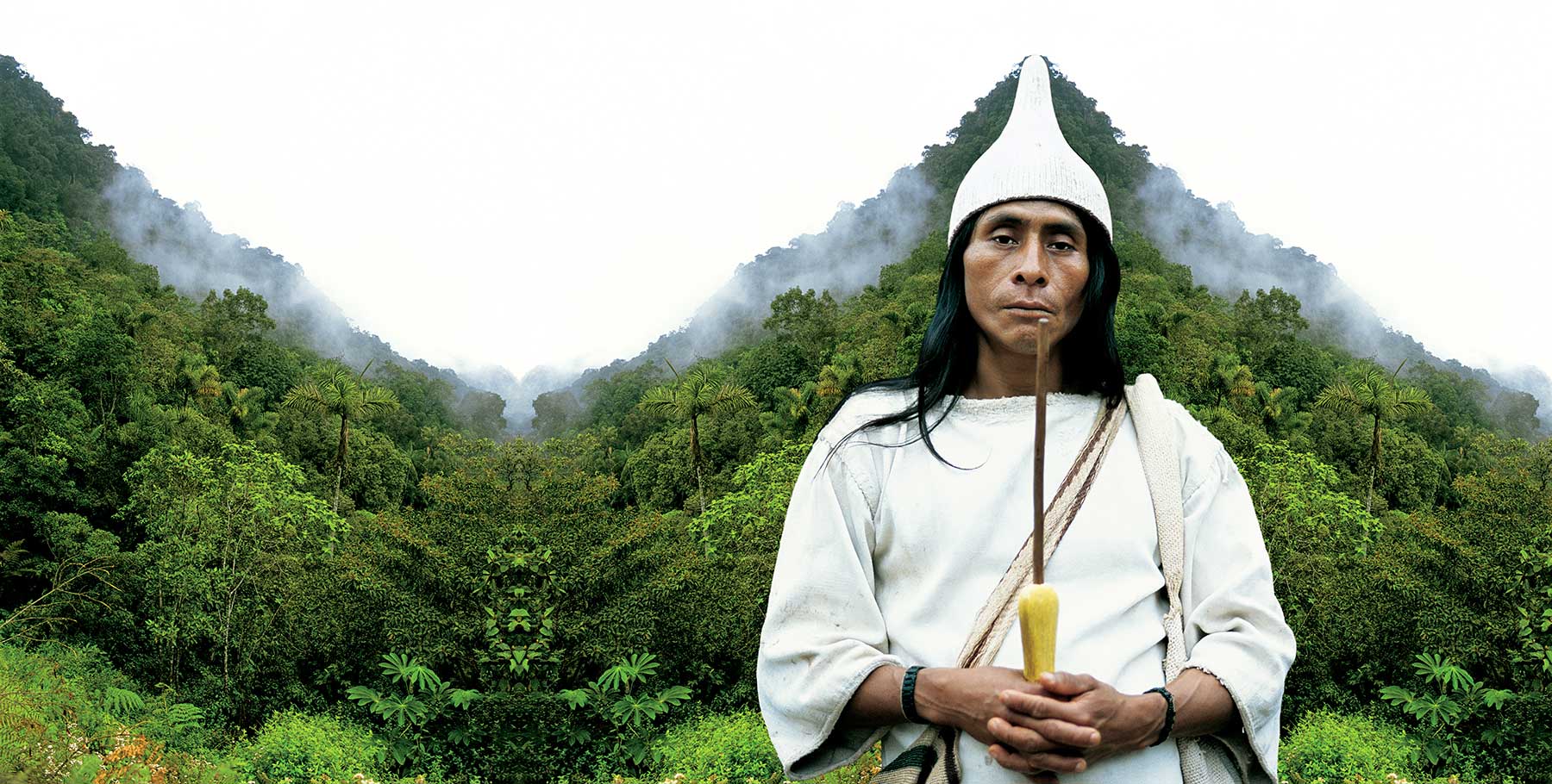 indigenous man in front of forested mountains