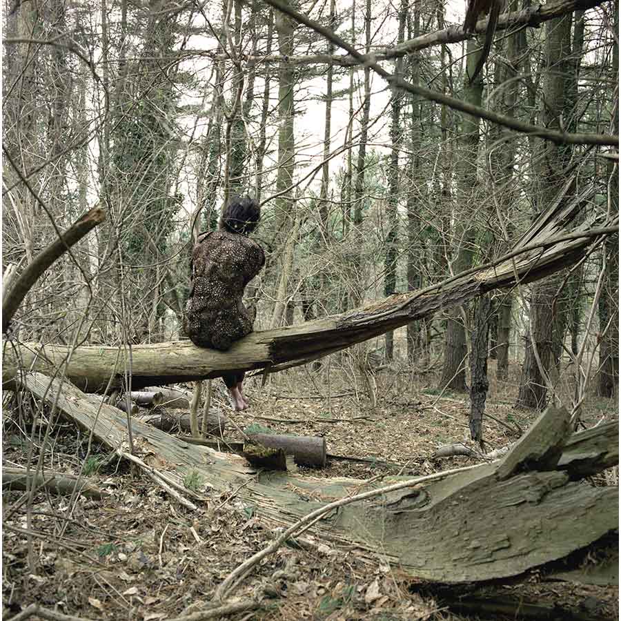 woman covered with feathers sitting in a forest