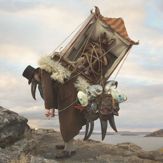 stooped salesman wearing bird mask with masks and tent on back