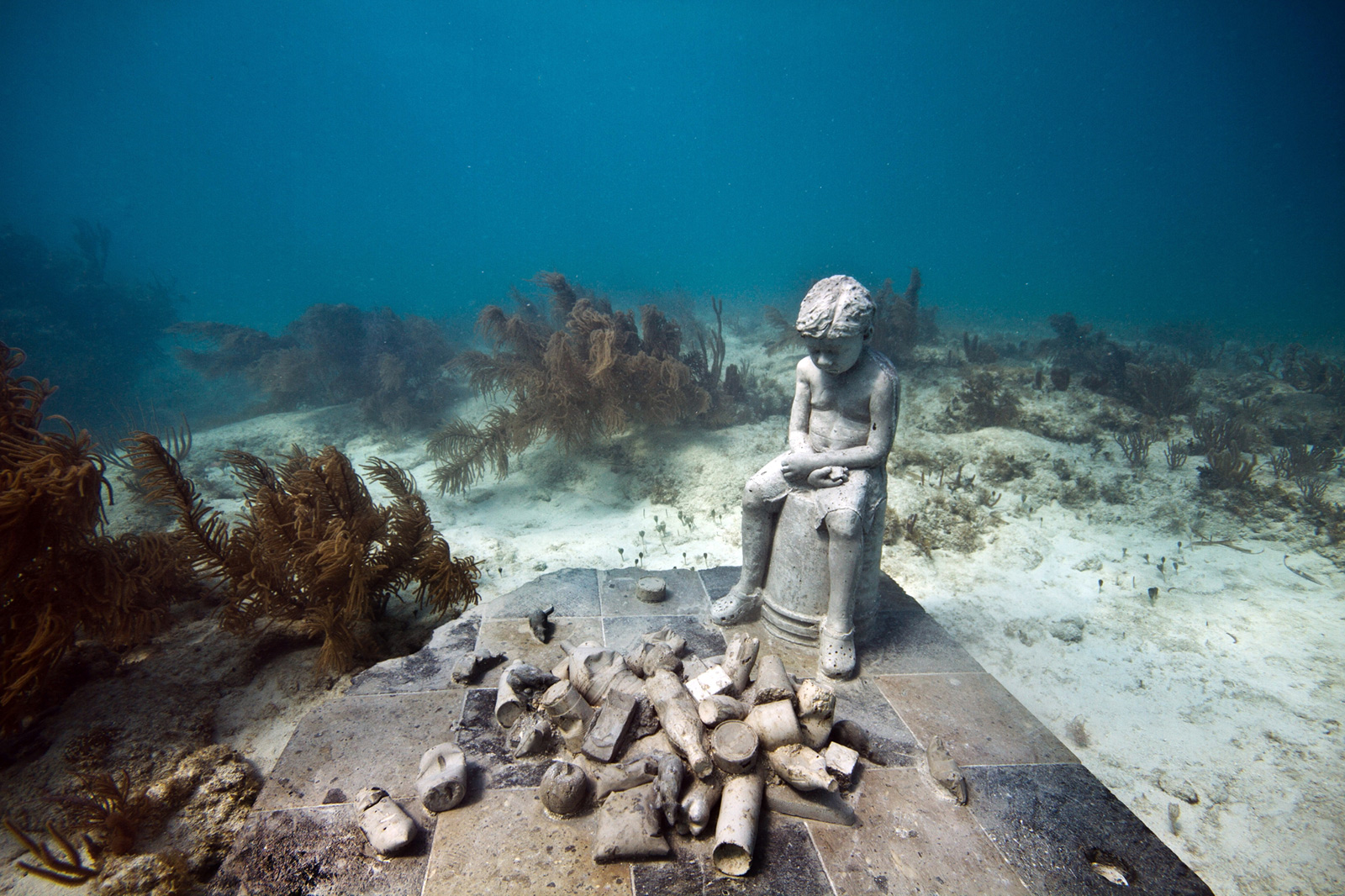 underwater sculpture of child and trash