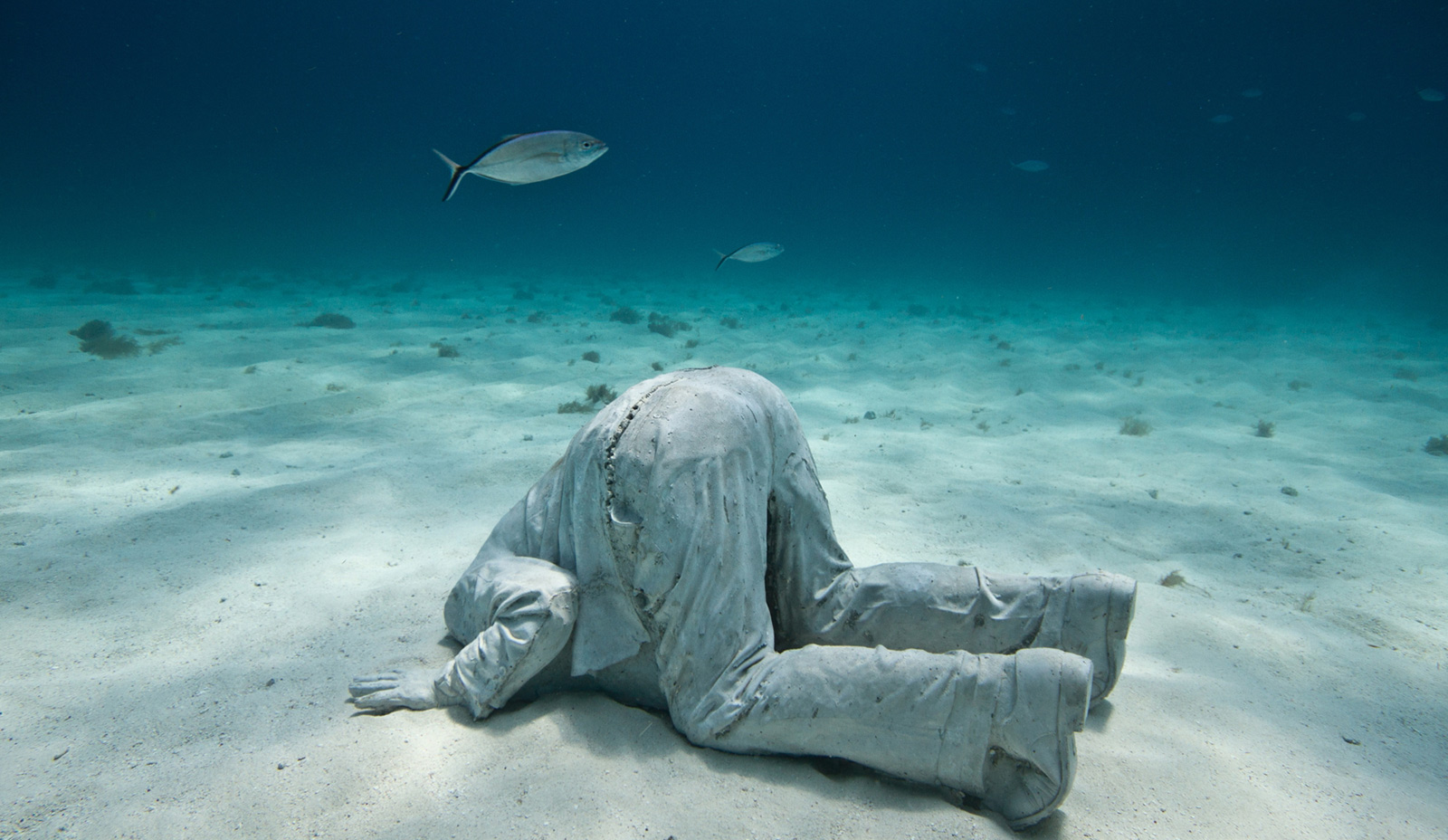 underwater sculpture of man with head in sand