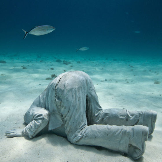 underwater sculpture of man with head in sand