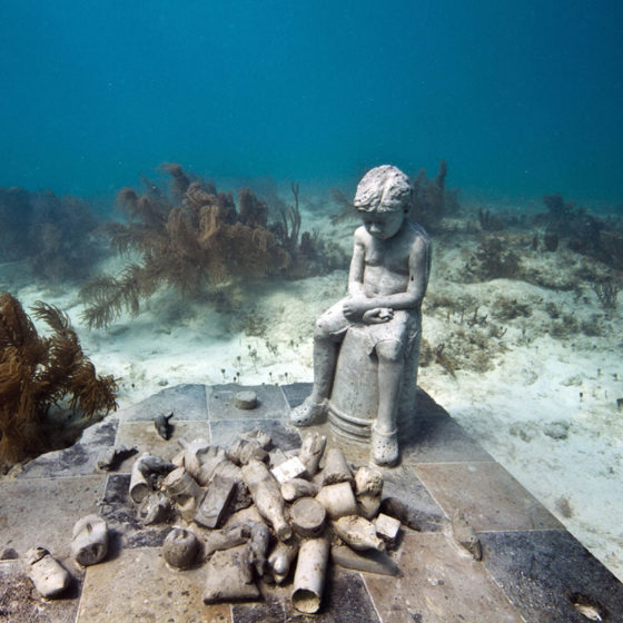 underwater sculpture of child and trash